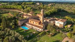Une vue aérienne d’un bâtiment historique doté d’une tour centrale, entouré d’une végétation luxuriante et d’une piscine.