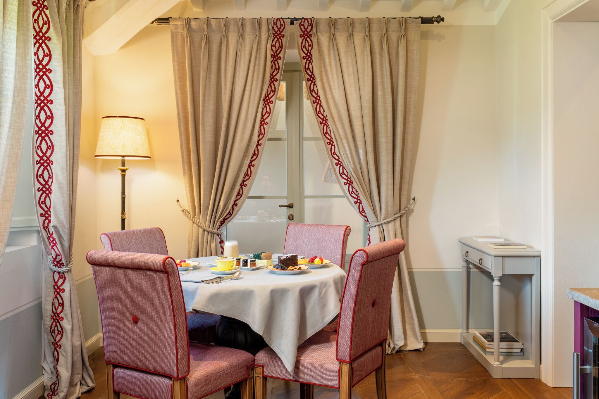 Un coin repas avec une table dressée pour quatre personnes, entourée de chaises, d’une lampe et d’une petite table d’appoint.