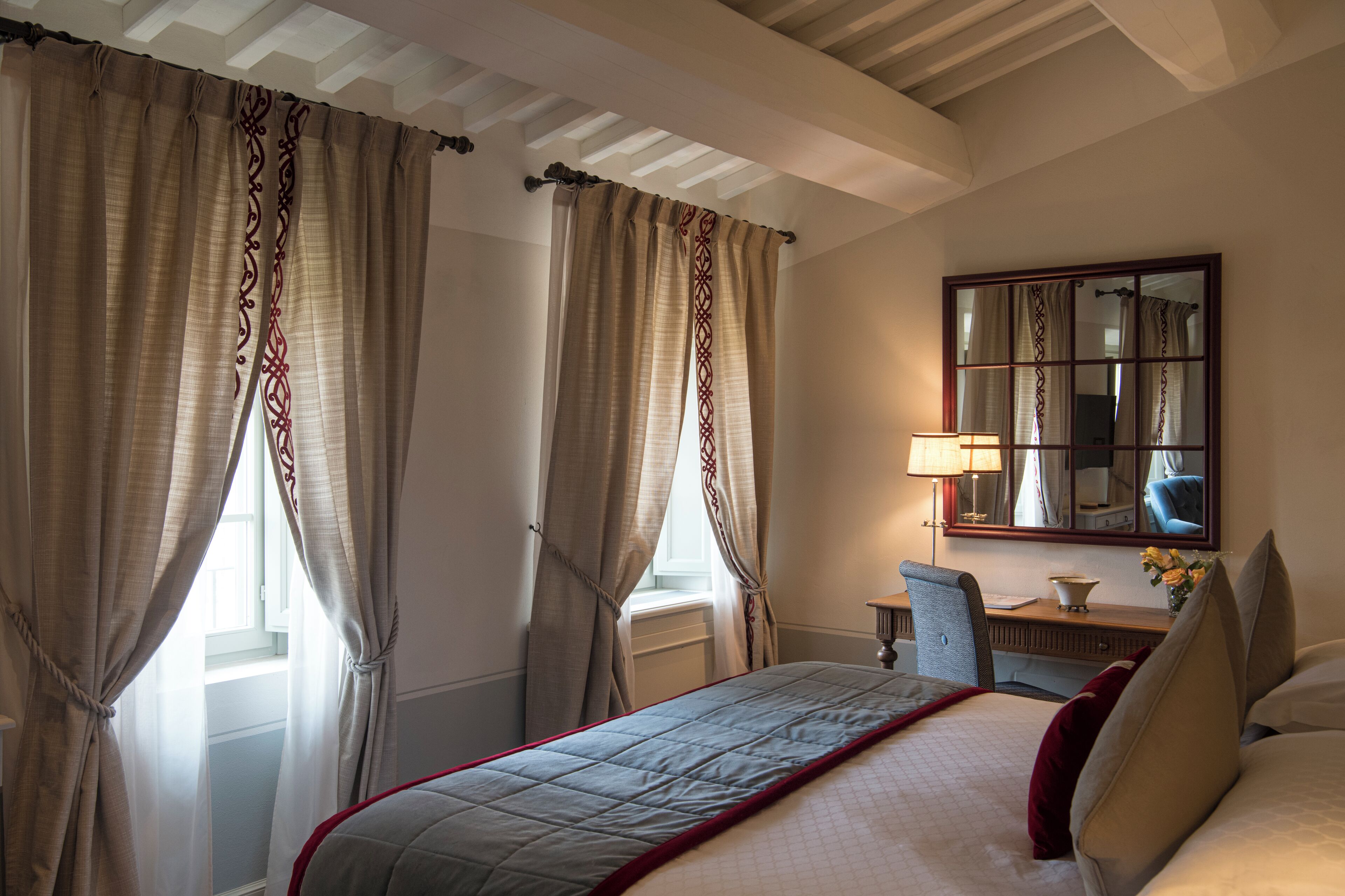 Una camera d'albergo con un letto, una scrivania, una sedia, una lampada e uno specchio.