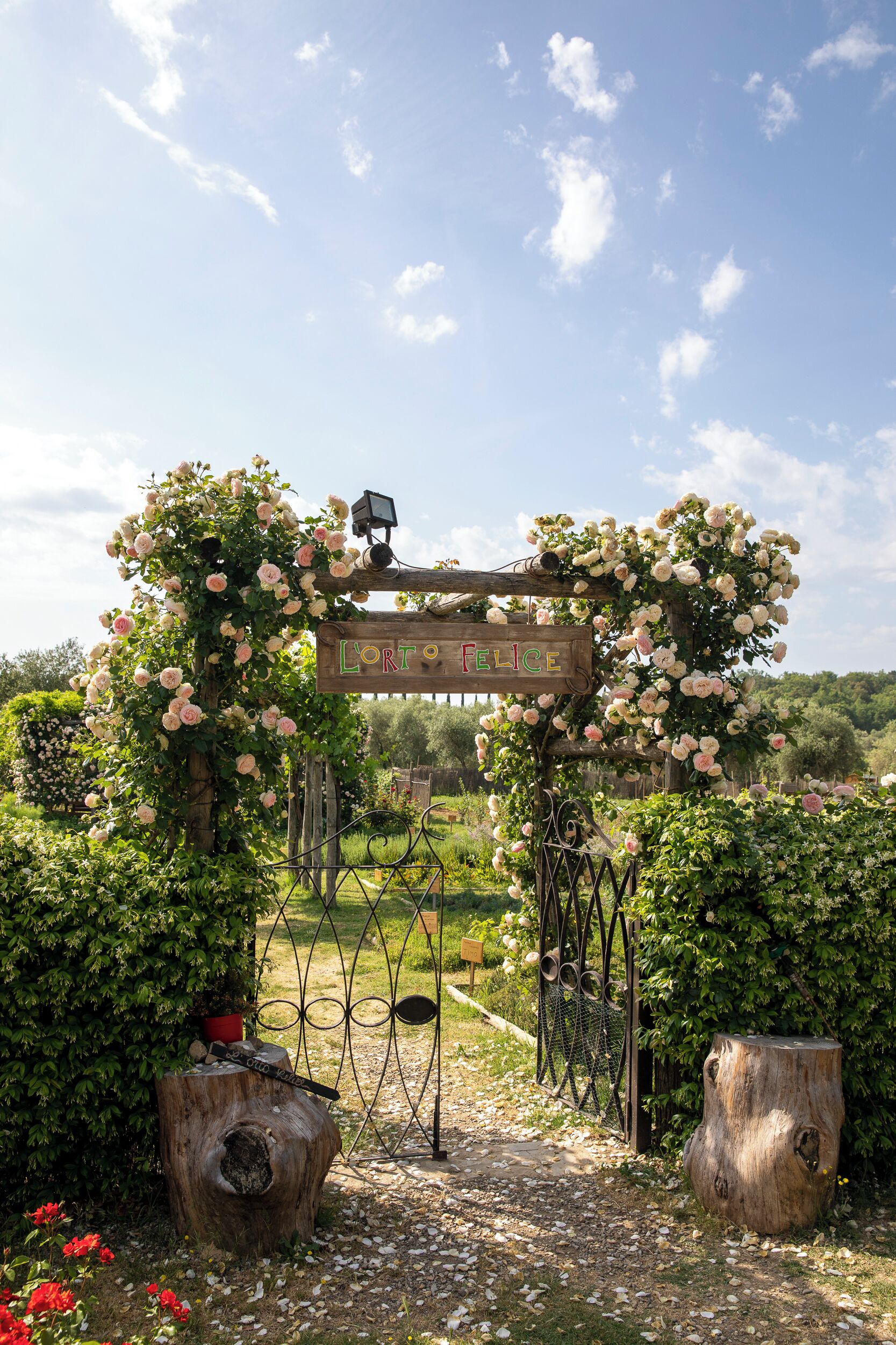 A wooden archway with a sign reading "LORTO FELICE" surrounded by lush greenery and flowers.