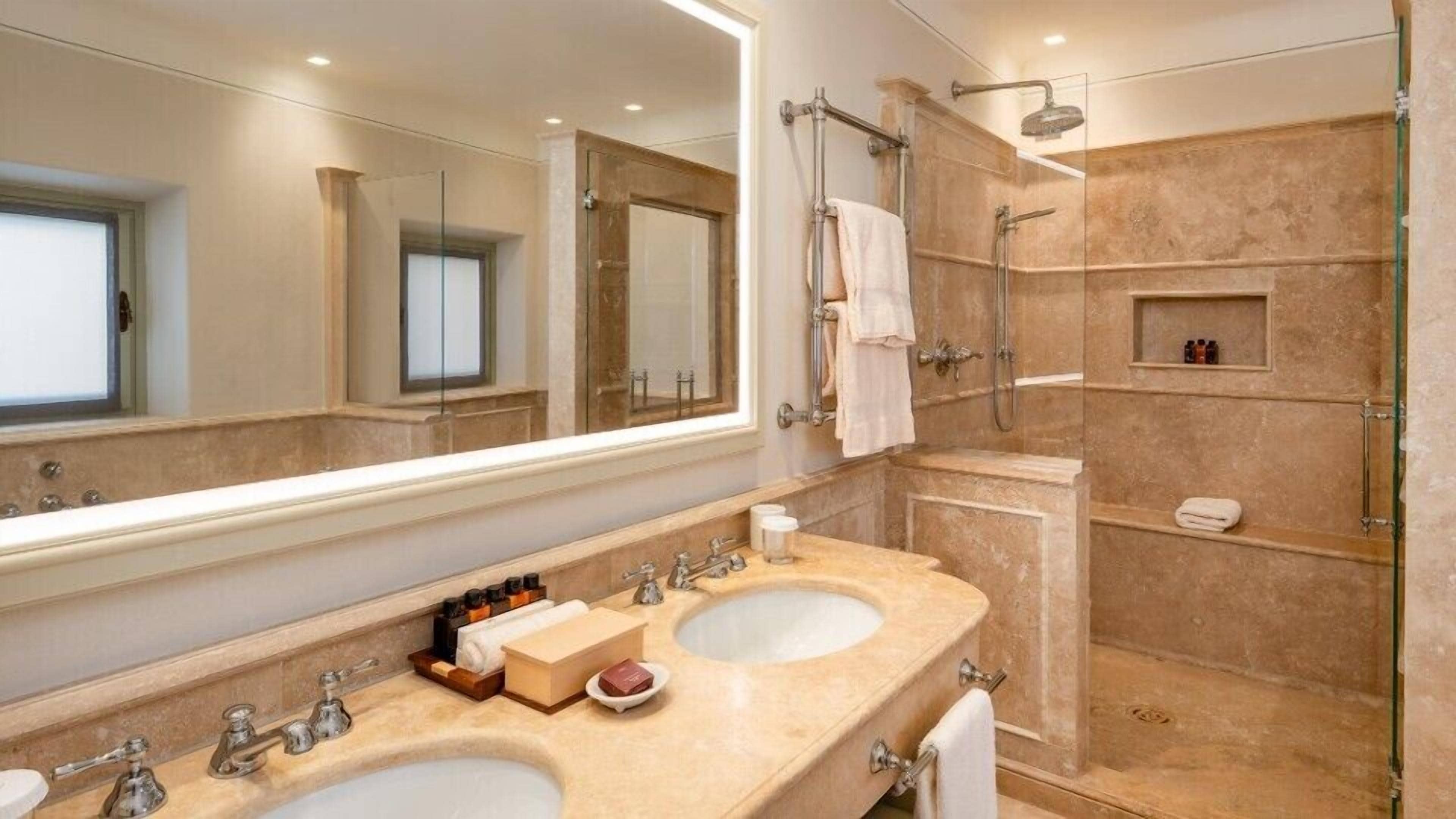 Un baño con dos lavamanos, un espejo grande, una ducha y un tocador con mampara de vidrio.