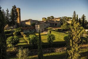 Un bâtiment historique doté d’une tour, entouré de jardins et d’arbres bien entretenus.