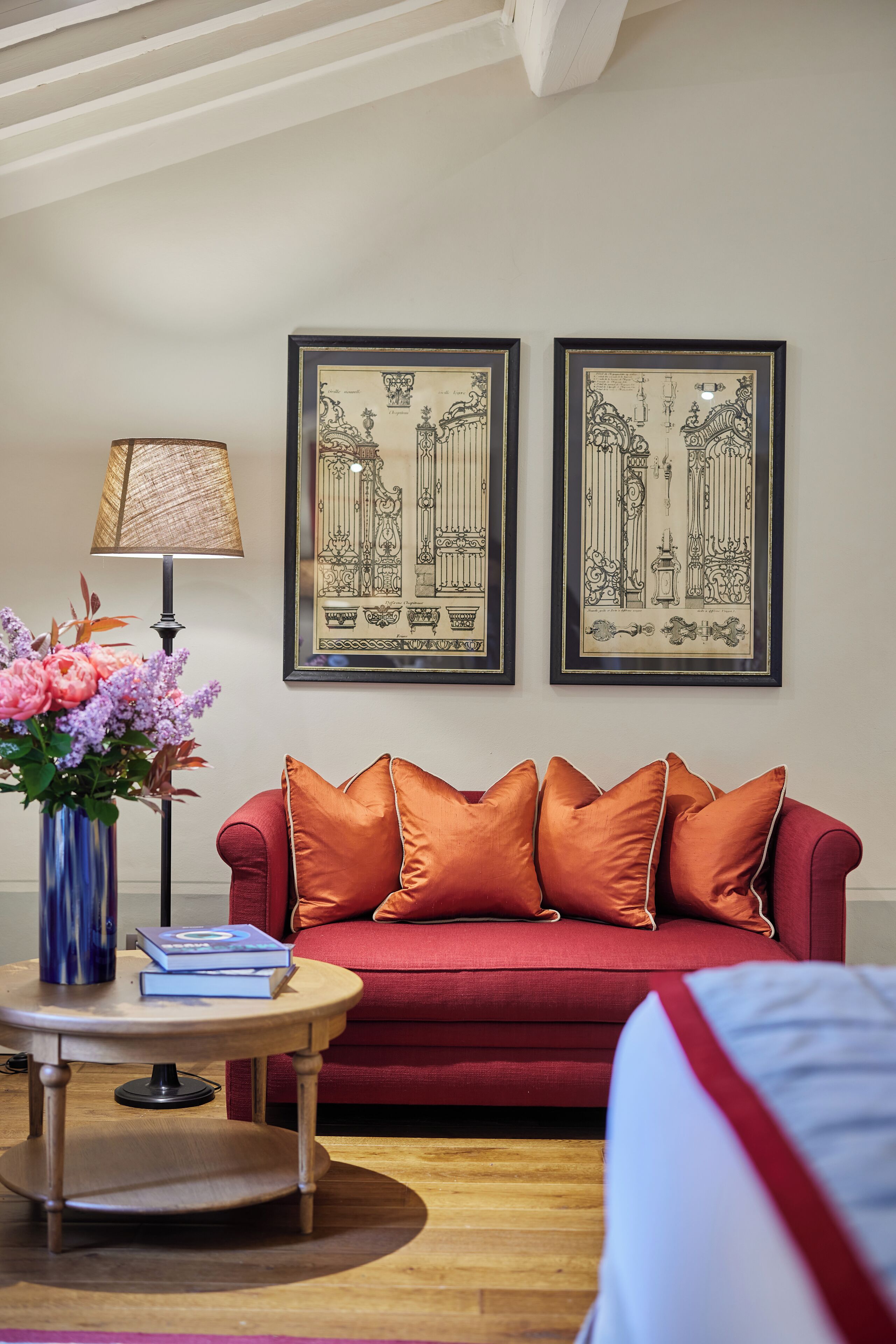 En rød sofa med orange puder, en blå vase med blomster, og to indrammede sort-hvide arkitekttegninger på væggen.