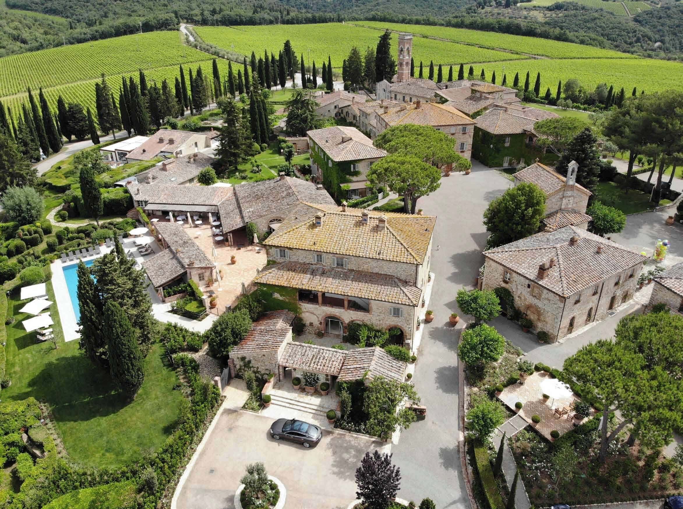 An aerial view of a rural estate with stone buildings, a swimming pool, and surrounding vineyards.