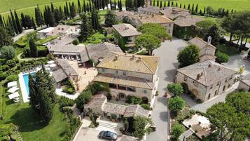 An aerial view of a rural estate with stone buildings, a swimming pool, and surrounding vineyards.
