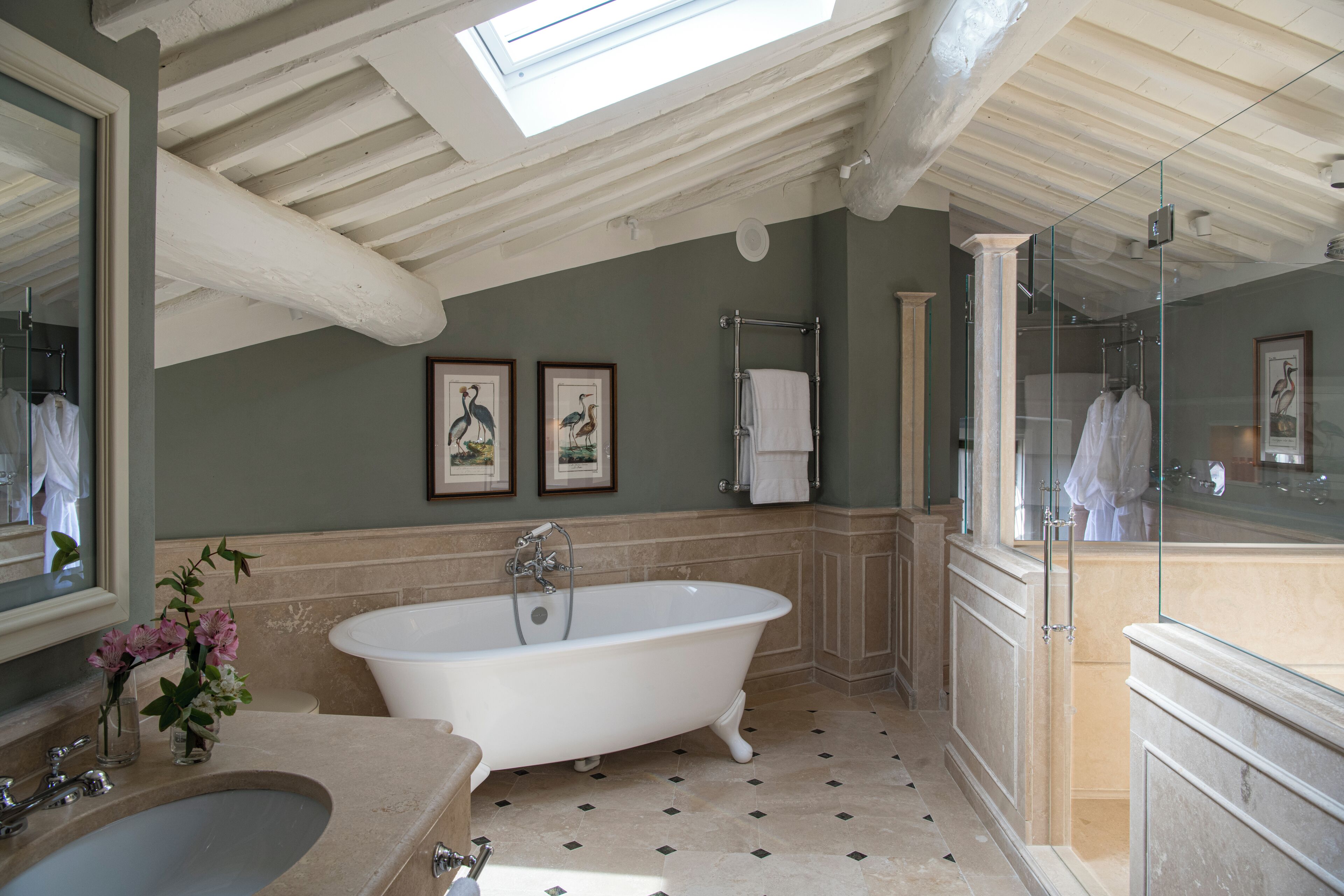 Une salle de bain avec une baignoire sur pieds, un grand miroir et une fenêtre de toit.