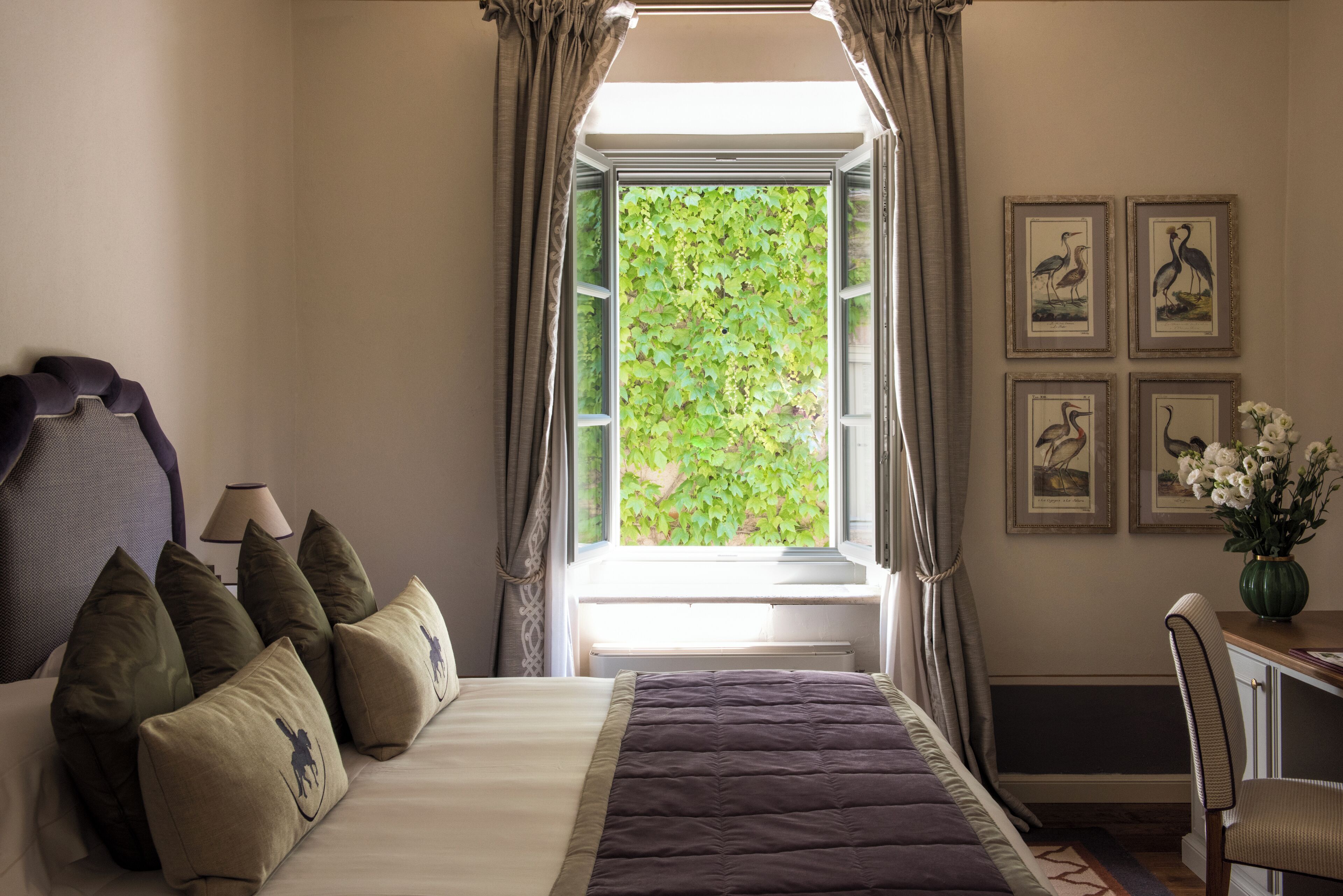 A bedroom with a bed, pillows, a desk, a chair, a lamp, and framed pictures on the wall.