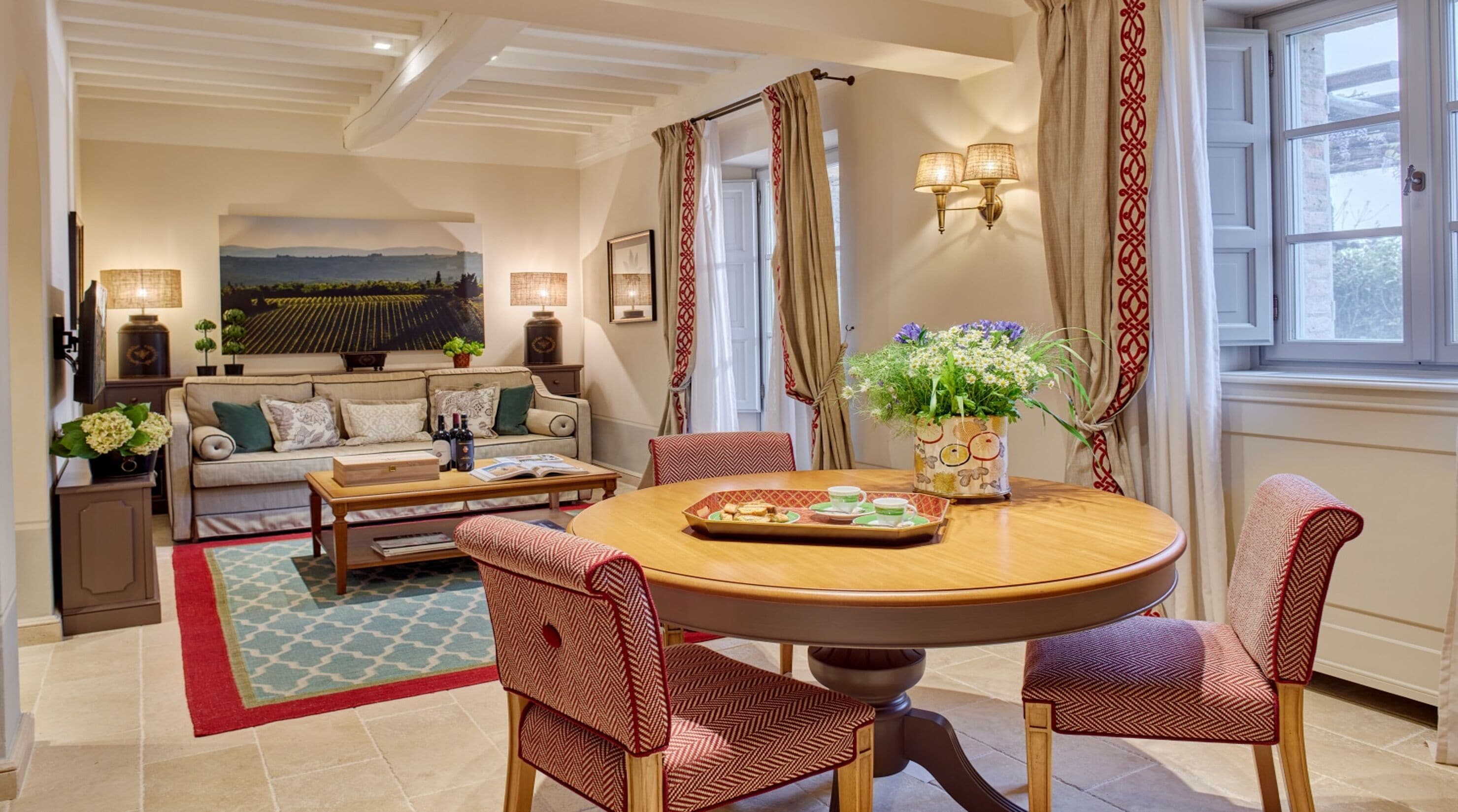 A well-furnished living room with a round dining table, red patterned chairs, a sofa, and a coffee table.
