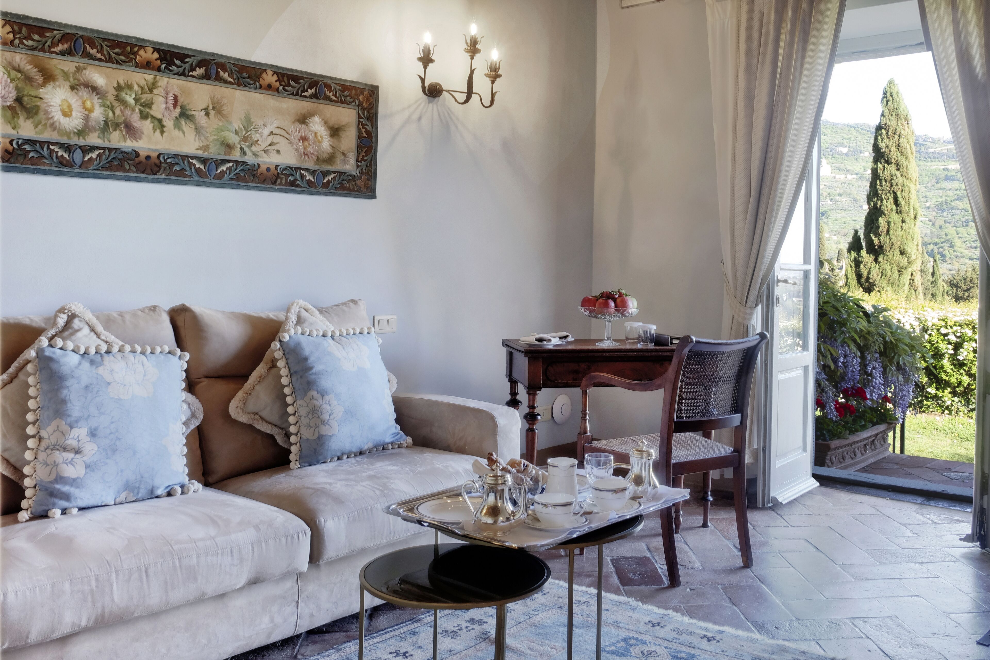 Uma sala de estar acolhedora com sofá, mesa de jantar posta para chá, um lustre e vista para o campo.