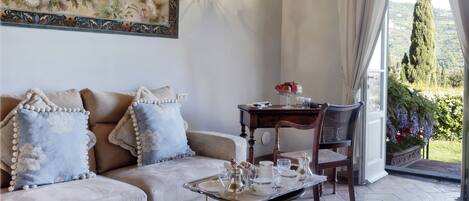 Uma sala de estar acolhedora com sofá, mesa de jantar posta para chá, um lustre e vista para o campo.