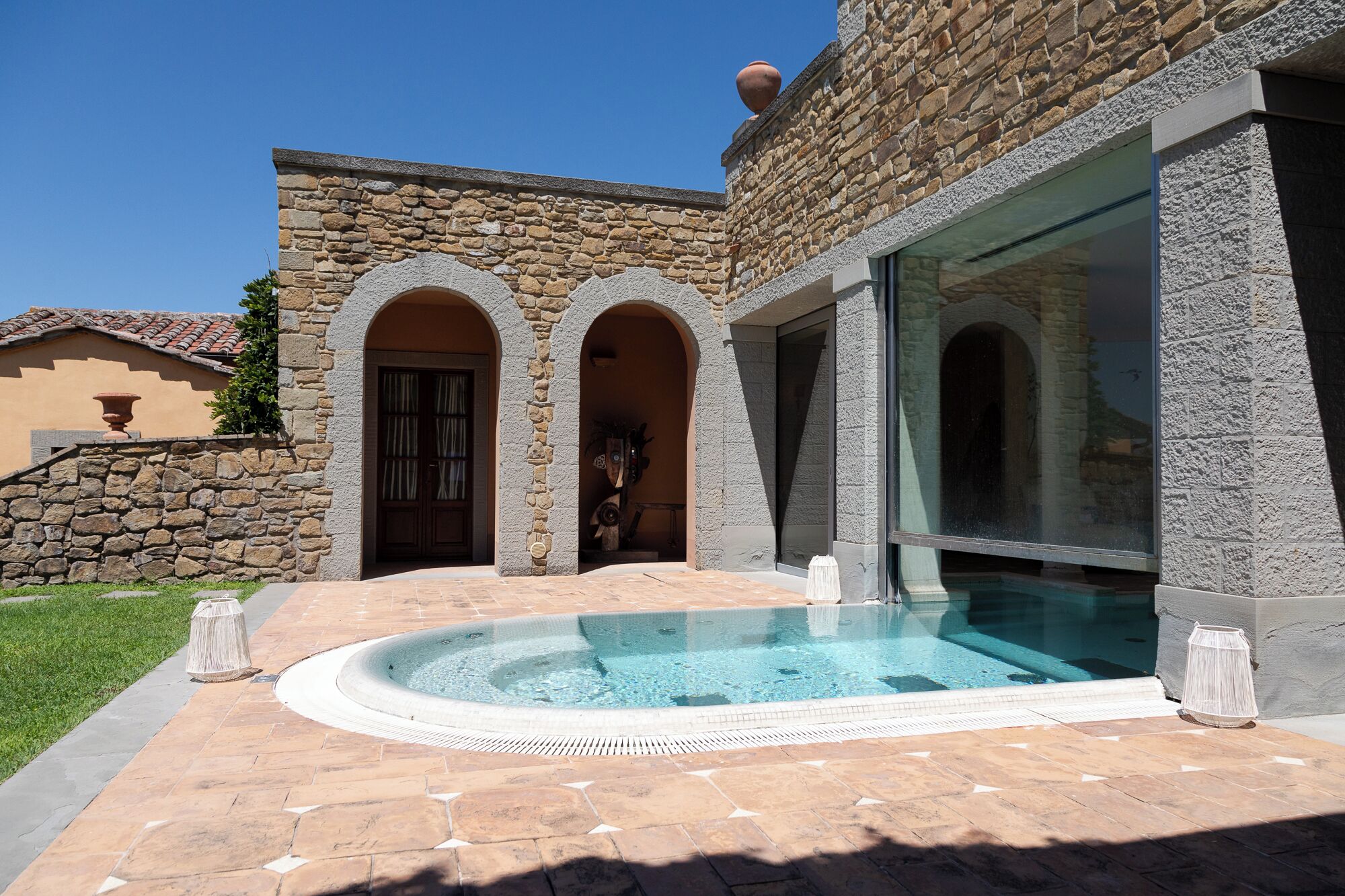 Un edificio de piedra con piscina, arcos y un amplio ventanal.