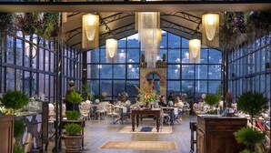 Un restaurante amplio y bien iluminado, con grandes ventanales, mesas de madera y plantas en macetas.