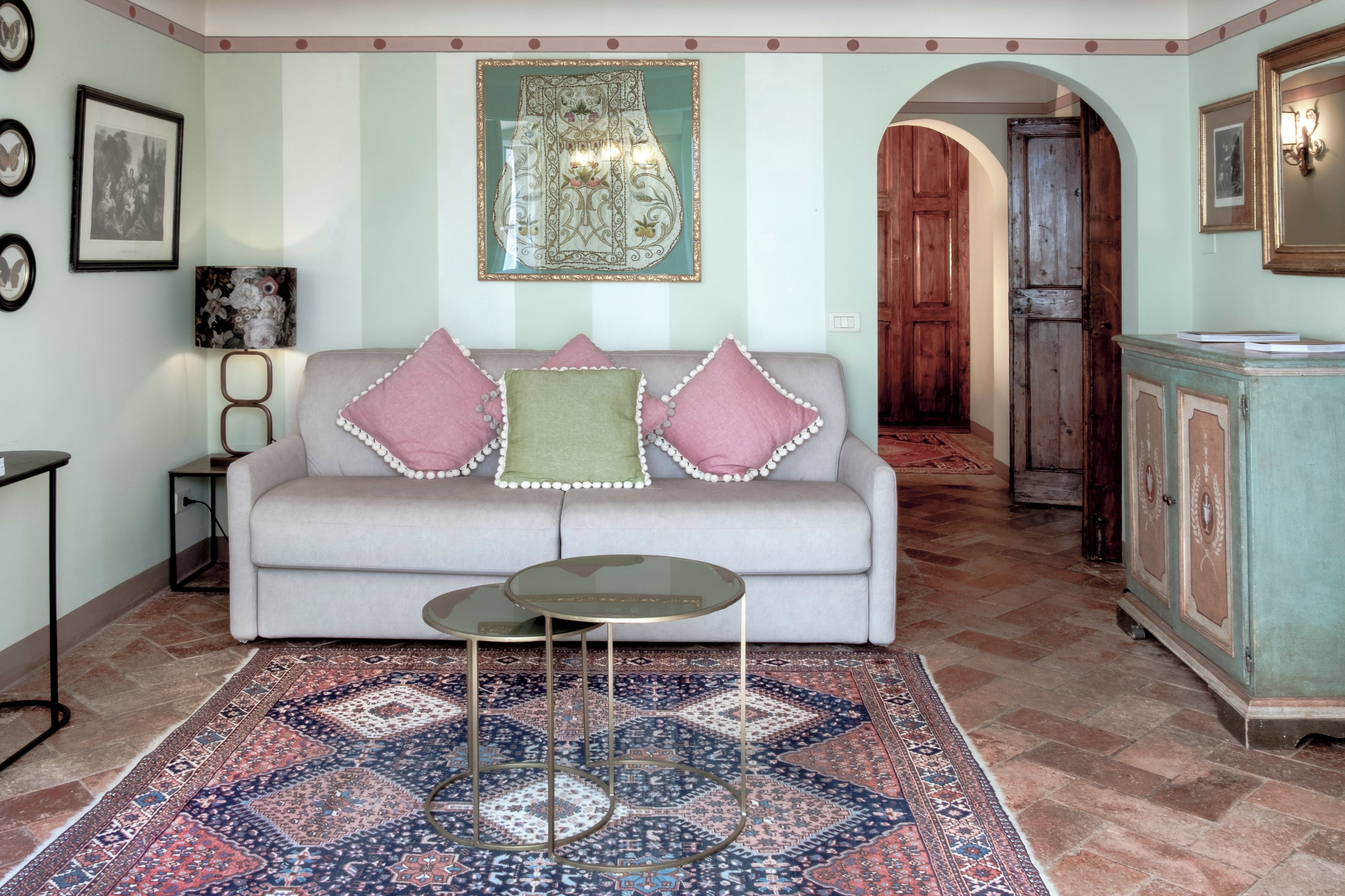Una sala de estar con un sofá, una mesa de centro, alfombras estampadas y un espejo decorativo.