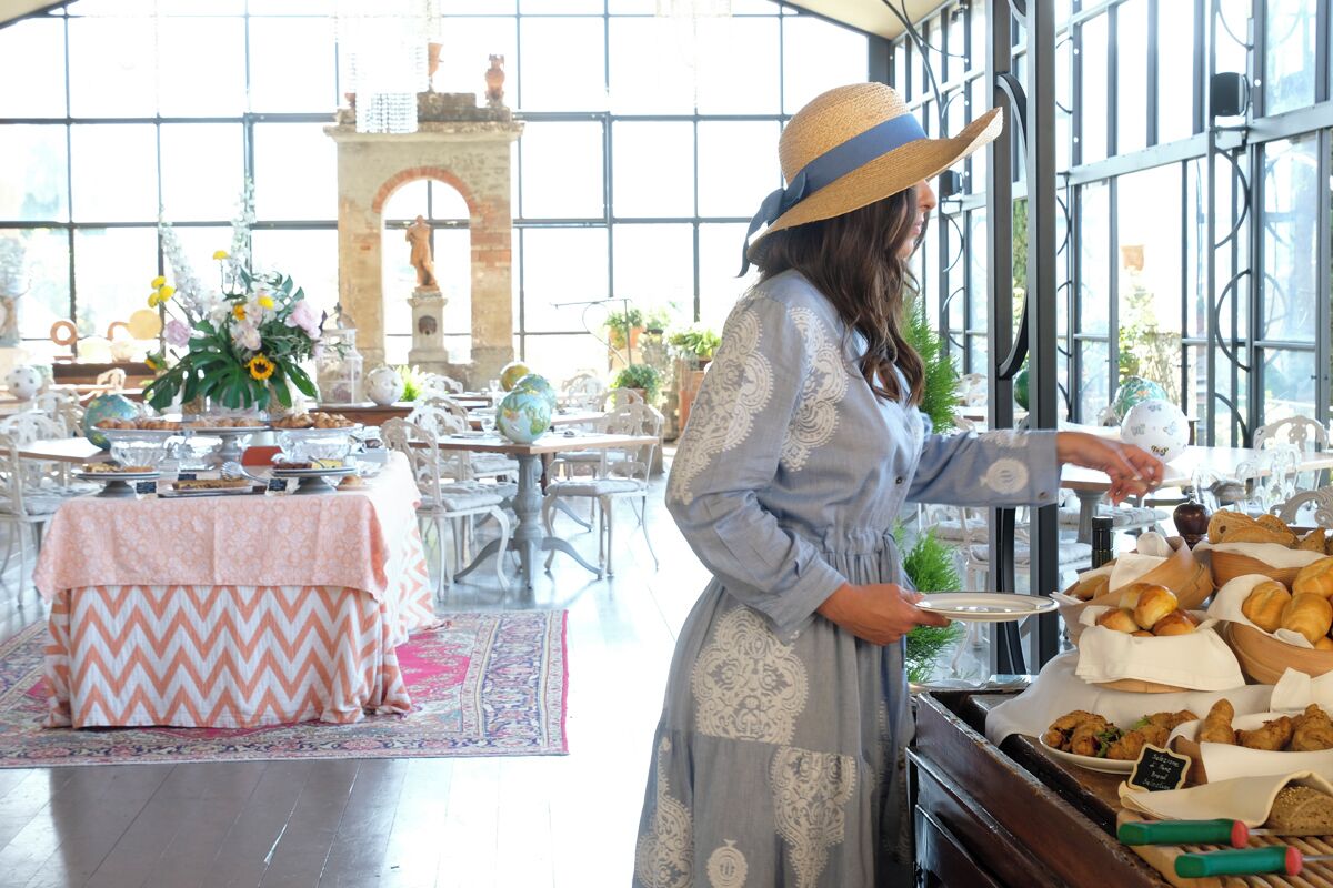 A woman serving food at a buffet table in a bright, open room with large windows and a decorative archway in the background.