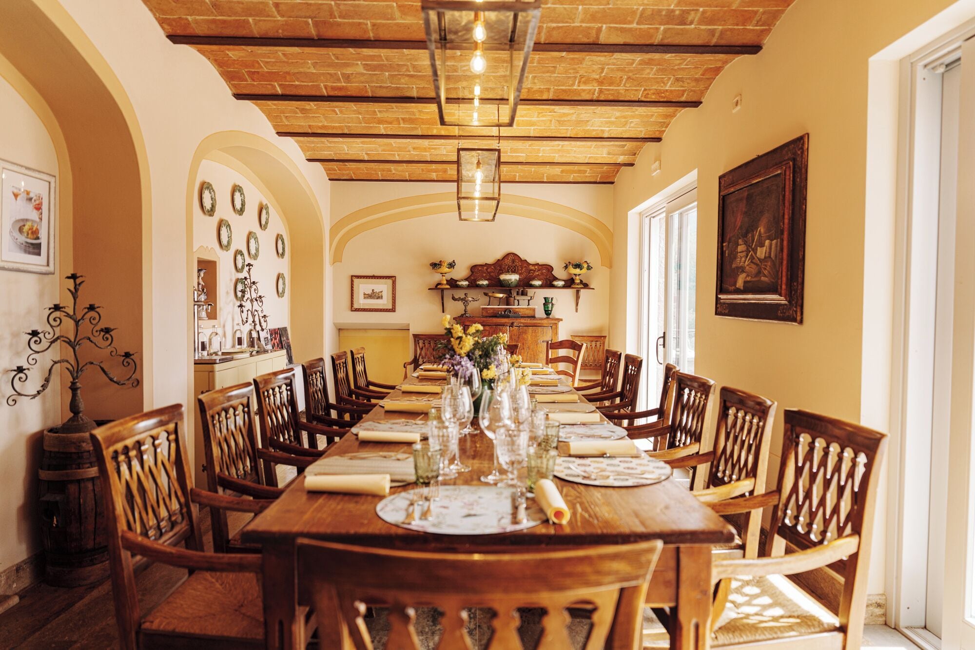 A long dining table with chairs, a brick ceiling, and a chandelier.
