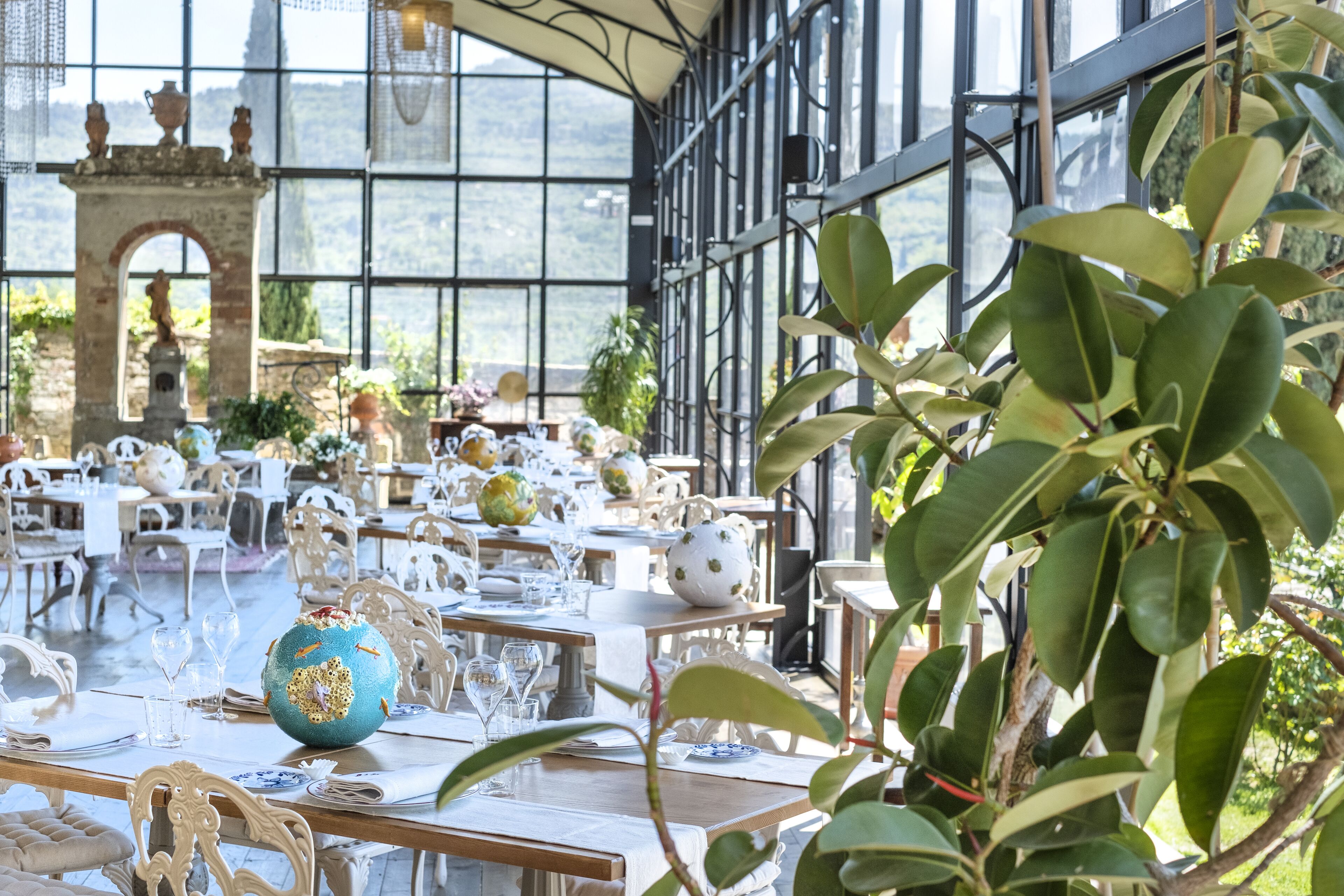 Un comedor interior amplio con mesas dispuestas para una comida, ventanas grandes y vistas al exterior.