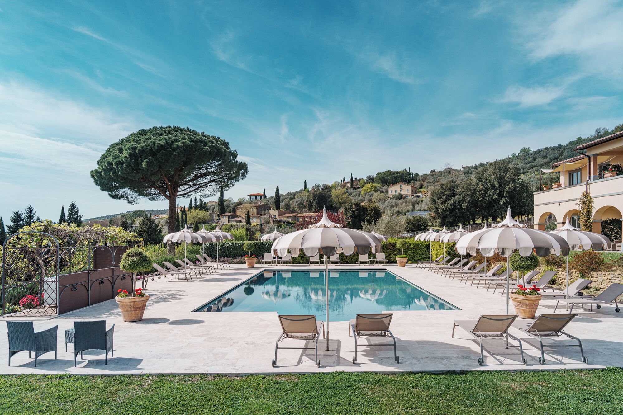 A pool area with lounge chairs and umbrellas, surrounded by greenery and a view of a hillside.