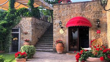Un bâtiment en pierre avec un auvent rouge, un escalier et des pots de fleurs rouges.