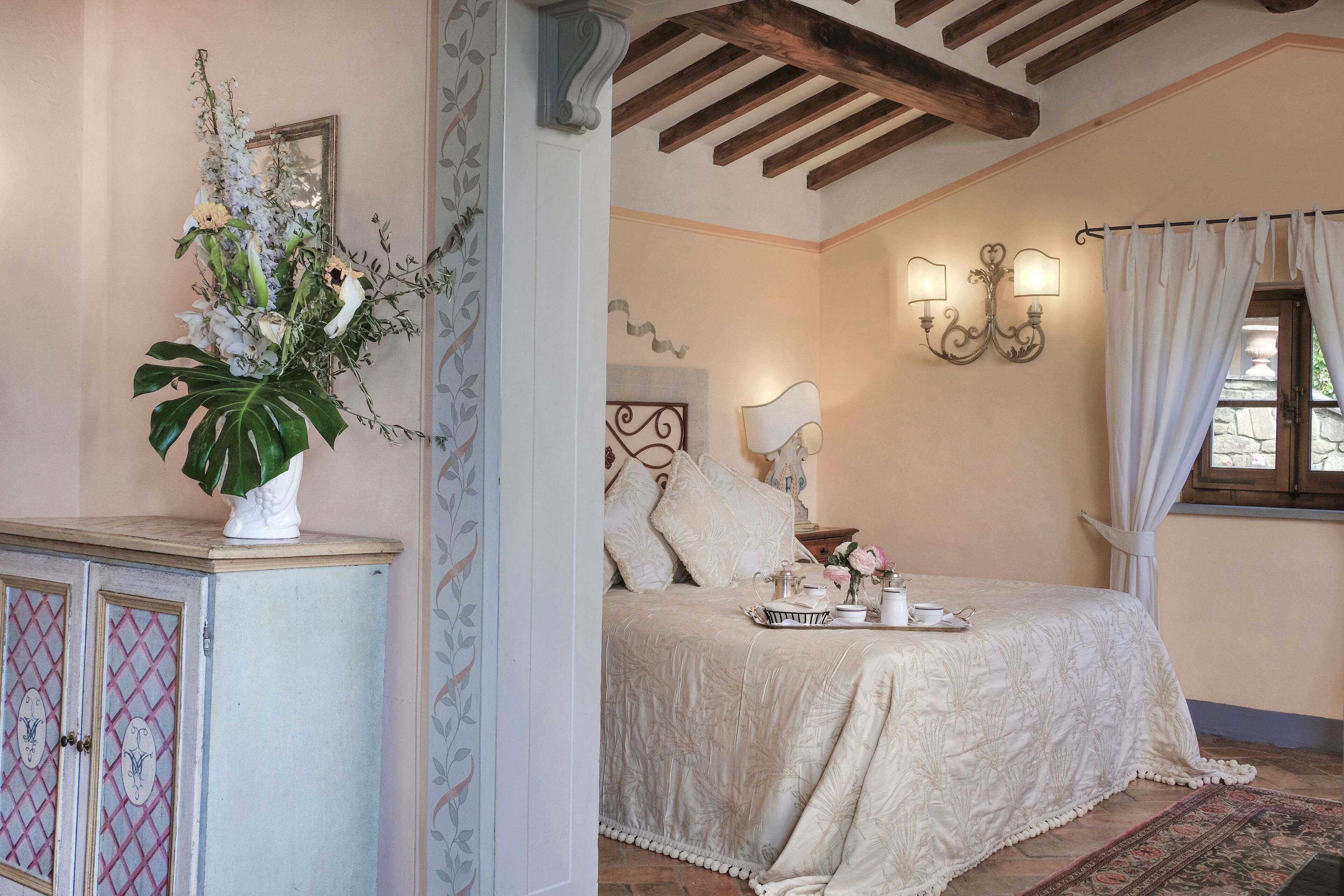 A bedroom with a bed, a nightstand, a vase of flowers, and a window with curtains.
