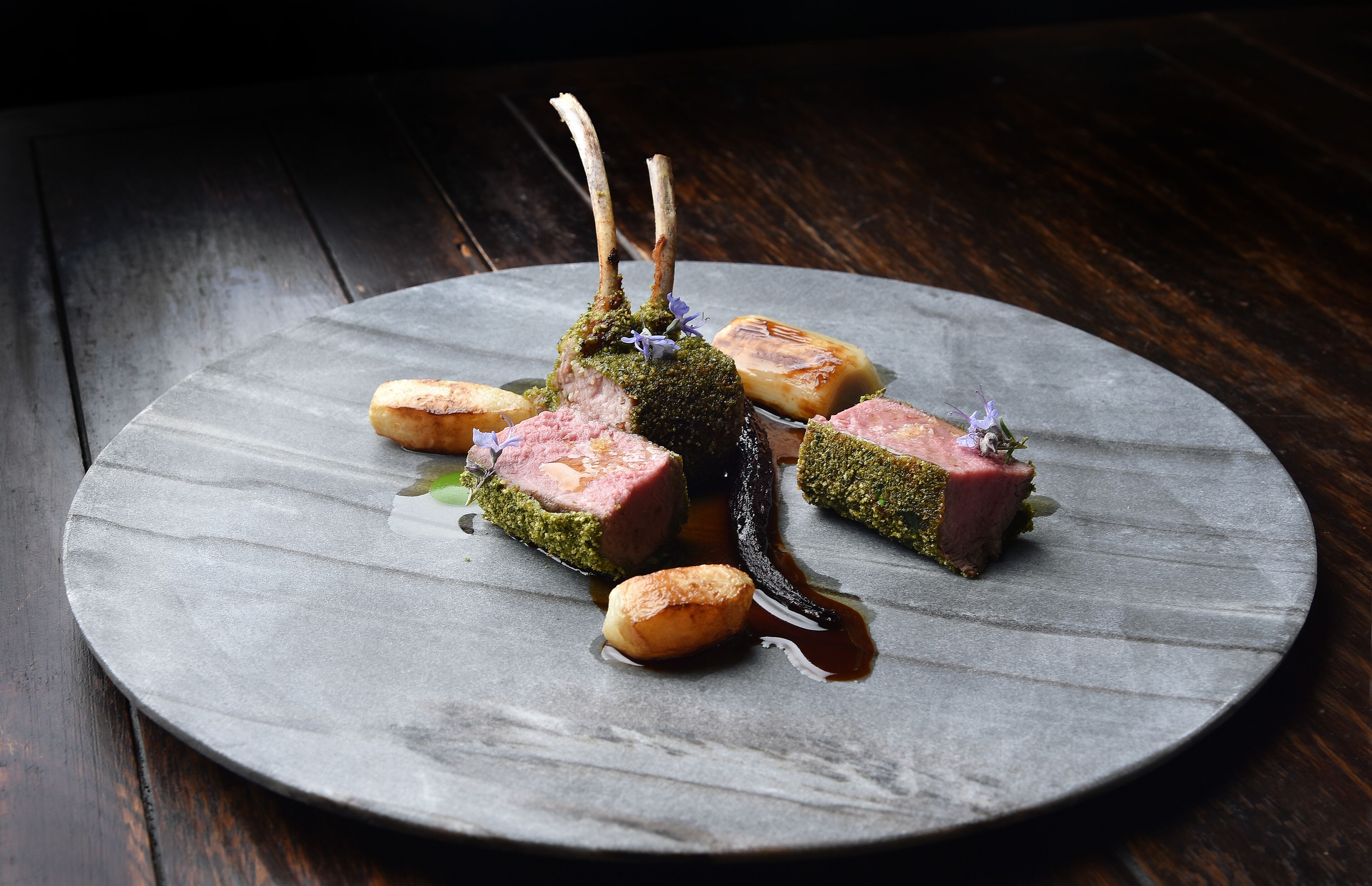 A round, slate-colored plate with a dish of meat, vegetables, and sauce.