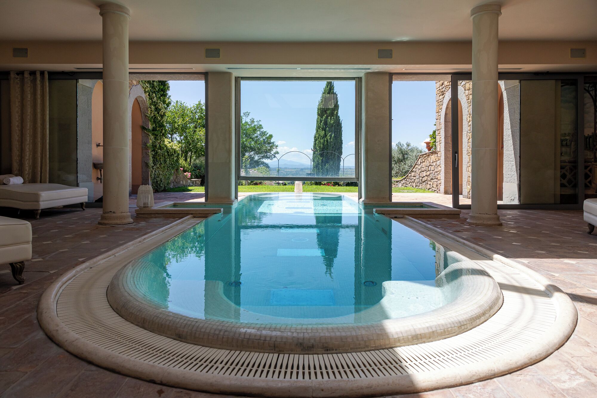 A large indoor swimming pool with a view of a stone building and trees.