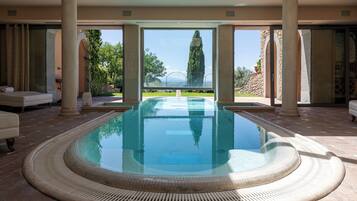 A large indoor swimming pool with a view of a stone building and trees.