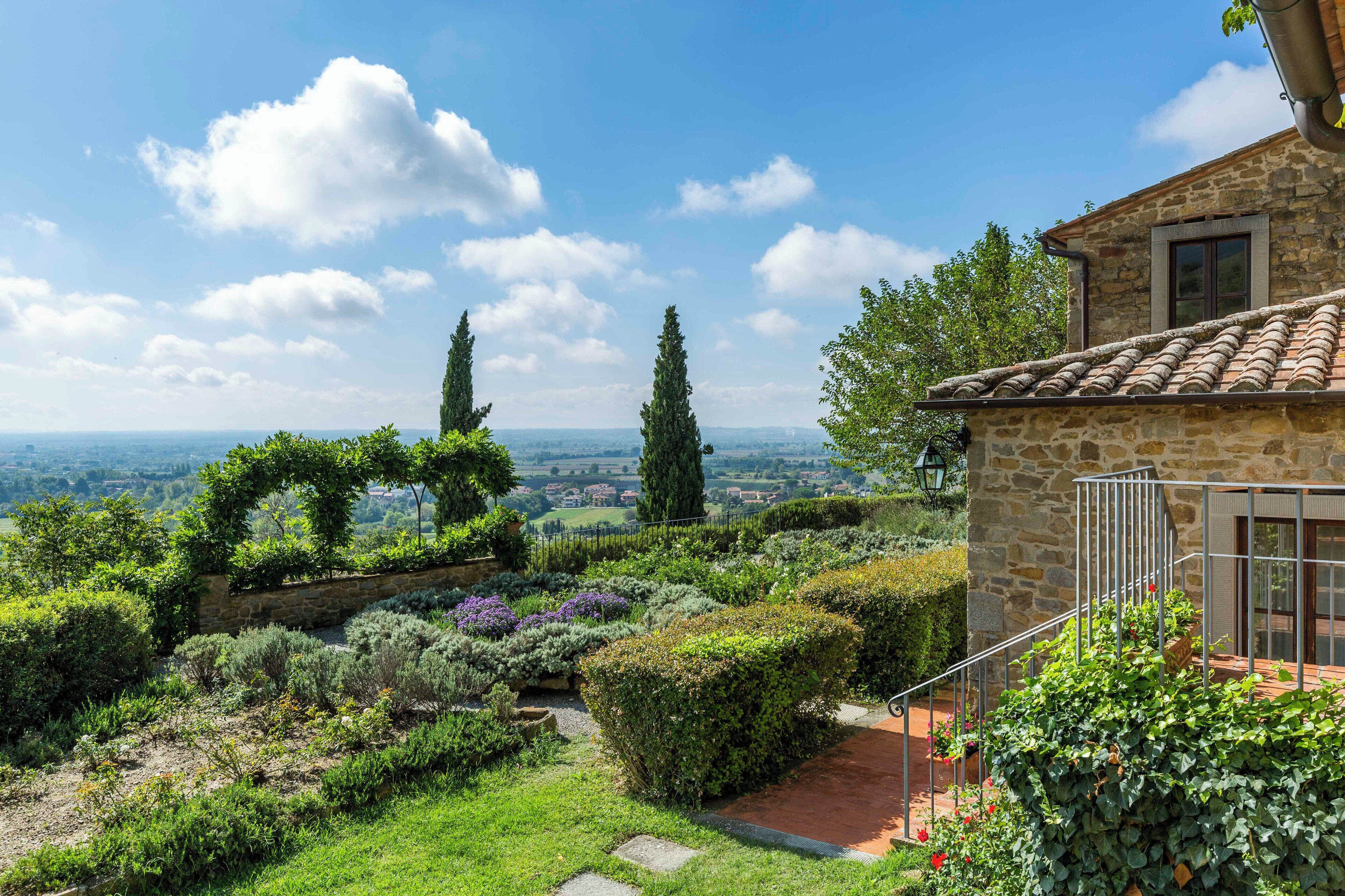 A stone house with a garden, a metal railing, and a view of the countryside.