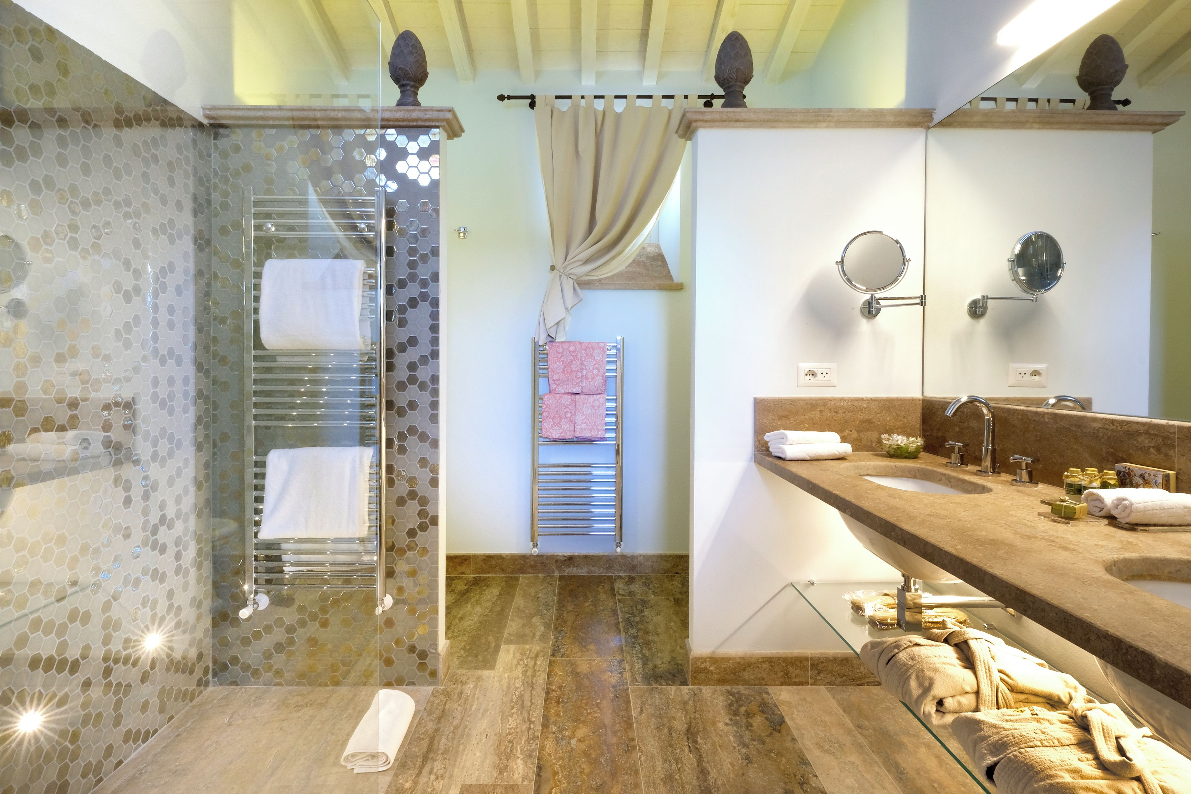 A bathroom with a glass shower enclosure, a vanity with a sink and mirror, and a towel rack with multiple towels.