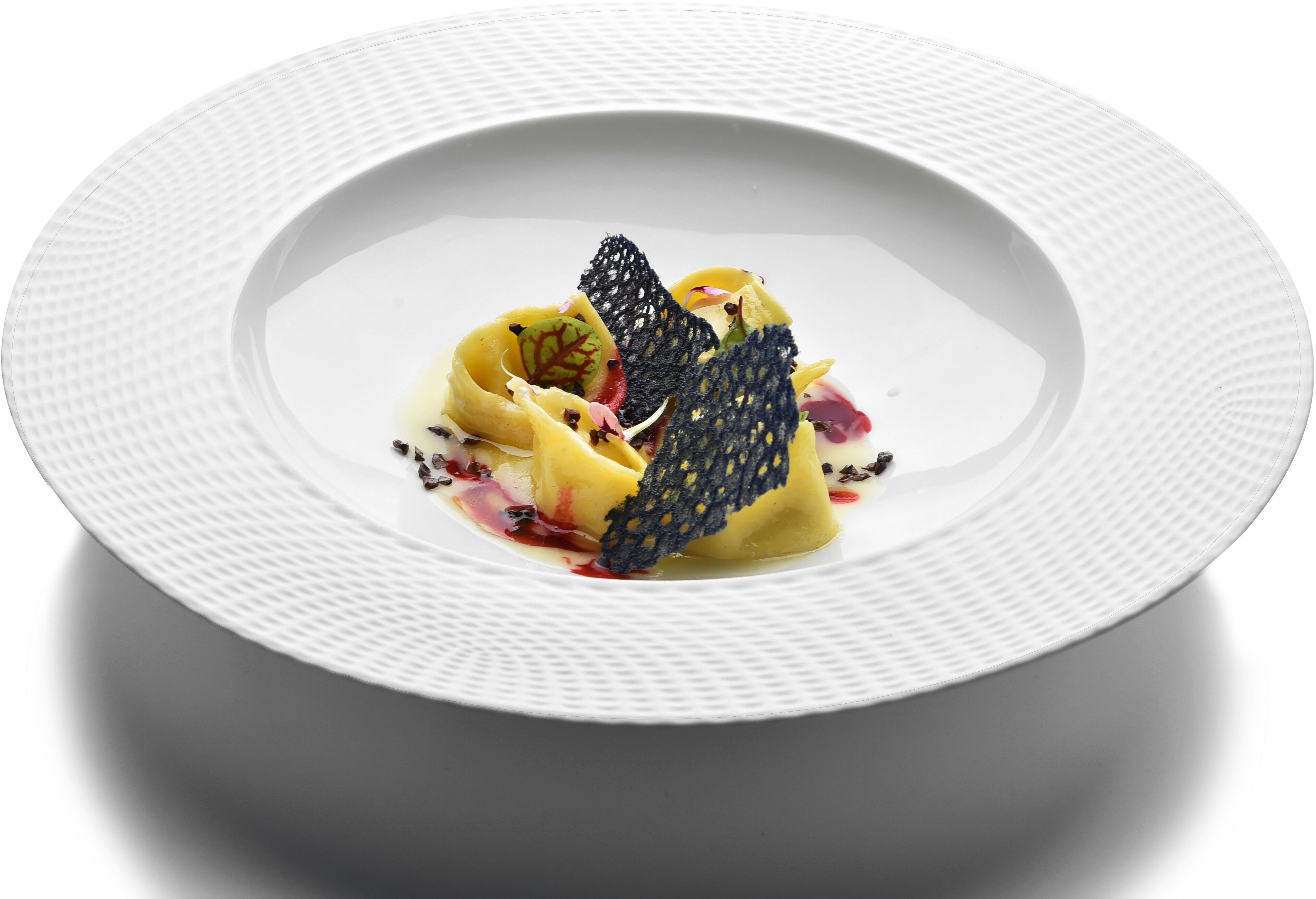 A white plate with a textured edge, containing a dessert with a dark, lace-like garnish, and a red sauce.