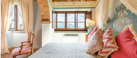 A bedroom with a large bed, a wooden chair, a window with a view, and a decorative wall.