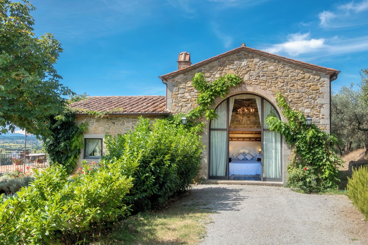 Un edificio de piedra con techo de tejas, un gran arco de entrada y una cama a la vista en su interior.