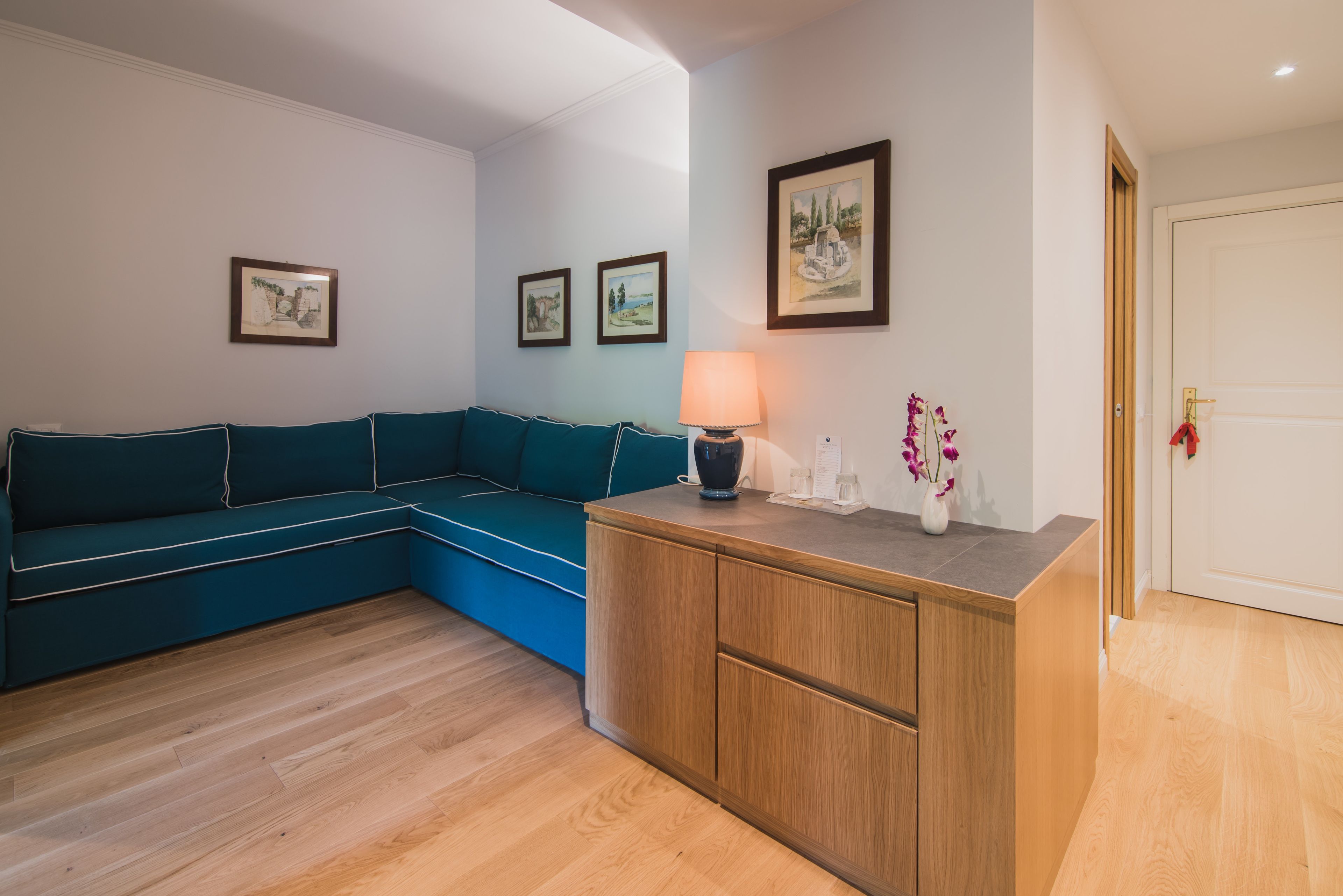 Ein Wohnzimmer mit einem petrolfarbenen Sofa, einer Holzkommode und gerahmten Kunstwerken an der Wand.
