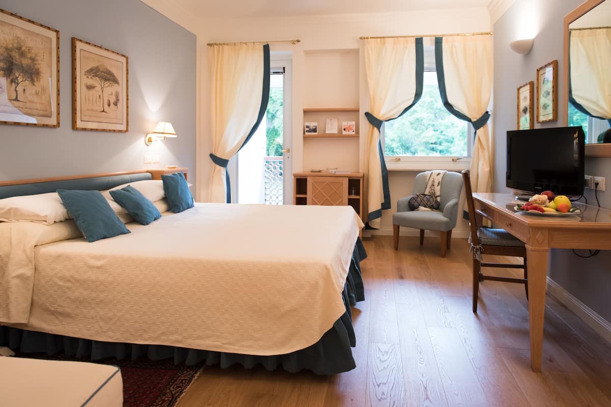 A bedroom with a bed, a desk with a chair, a television, and a window with curtains.