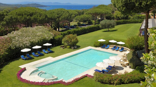 A rectangular swimming pool surrounded by a well-maintained lawn, with several lounge chairs and umbrellas. - Gallia Palace Hotel (Castiglione della Pescaia)