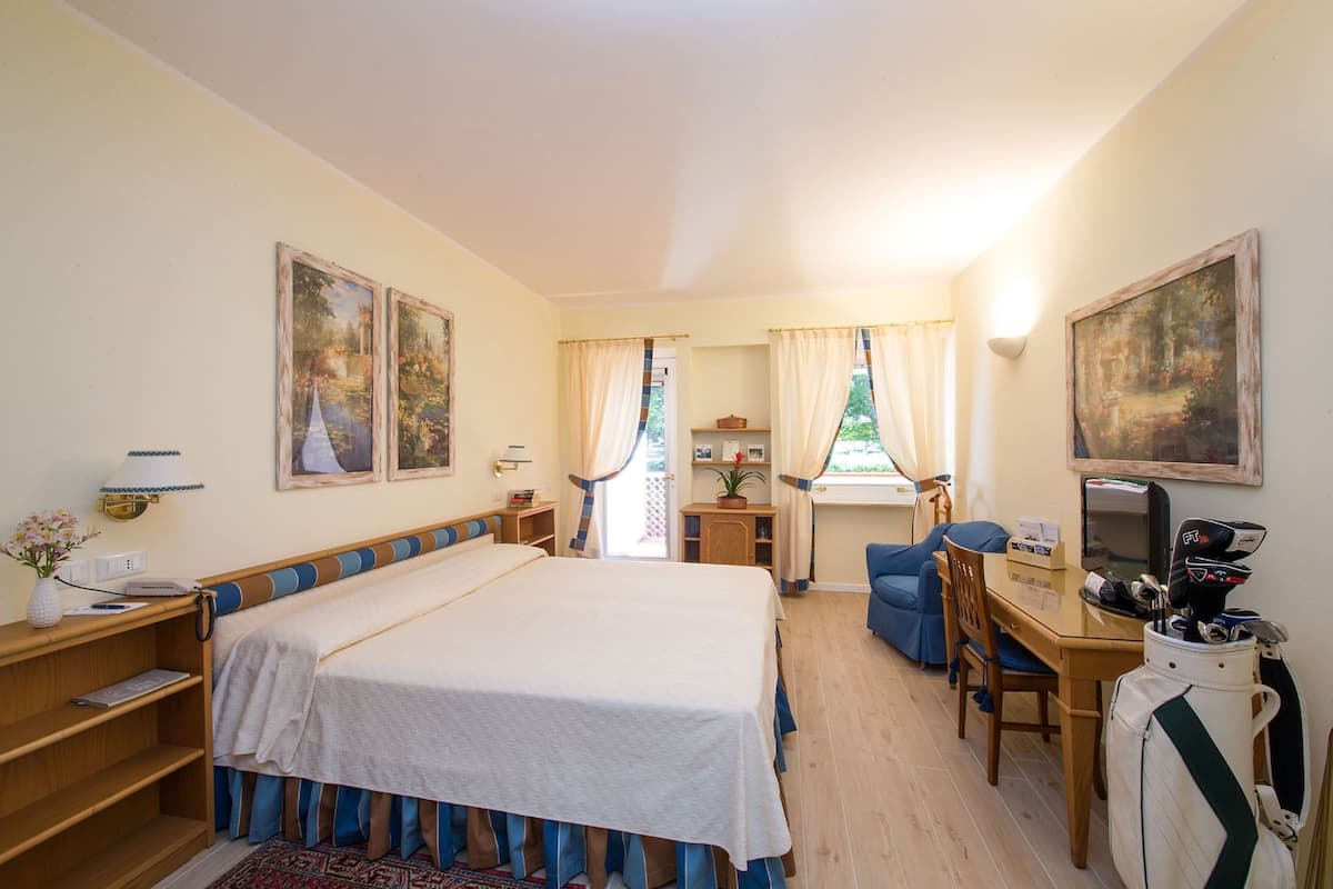 A hotel room with a bed, a desk, a chair, a TV, and a golf bag.
