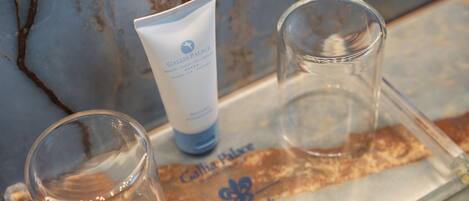 A bathroom counter with a marble wall, a tube of lotion, and two glasses.