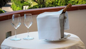 A table with two wine glasses and a bottle of champagne on a balcony overlooking a scenic view of the sea and greenery. - Gallia Palace Hotel (Castiglione della Pescaia)
