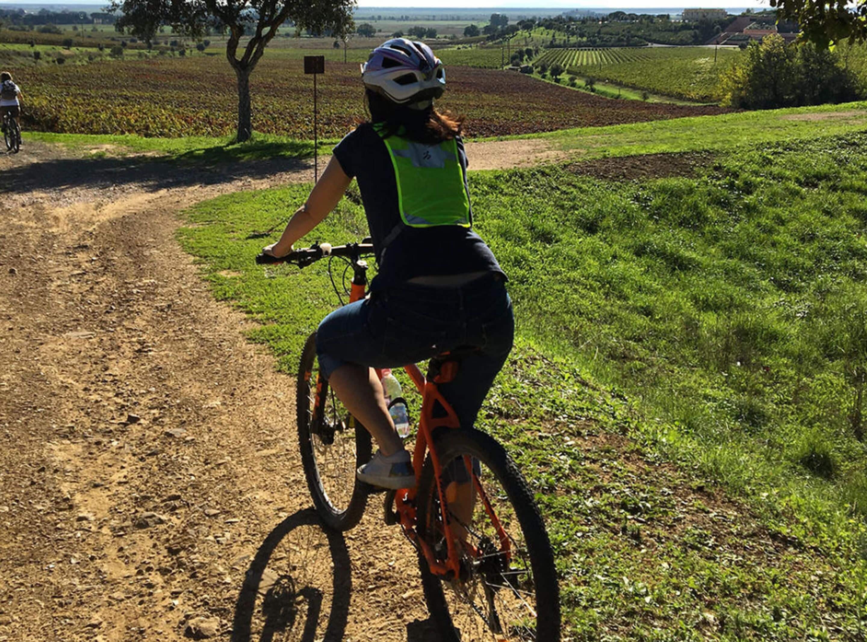 Une personne fait du vélo tout-terrain sur un chemin de terre dans une zone rurale, avec des champs et des arbres.