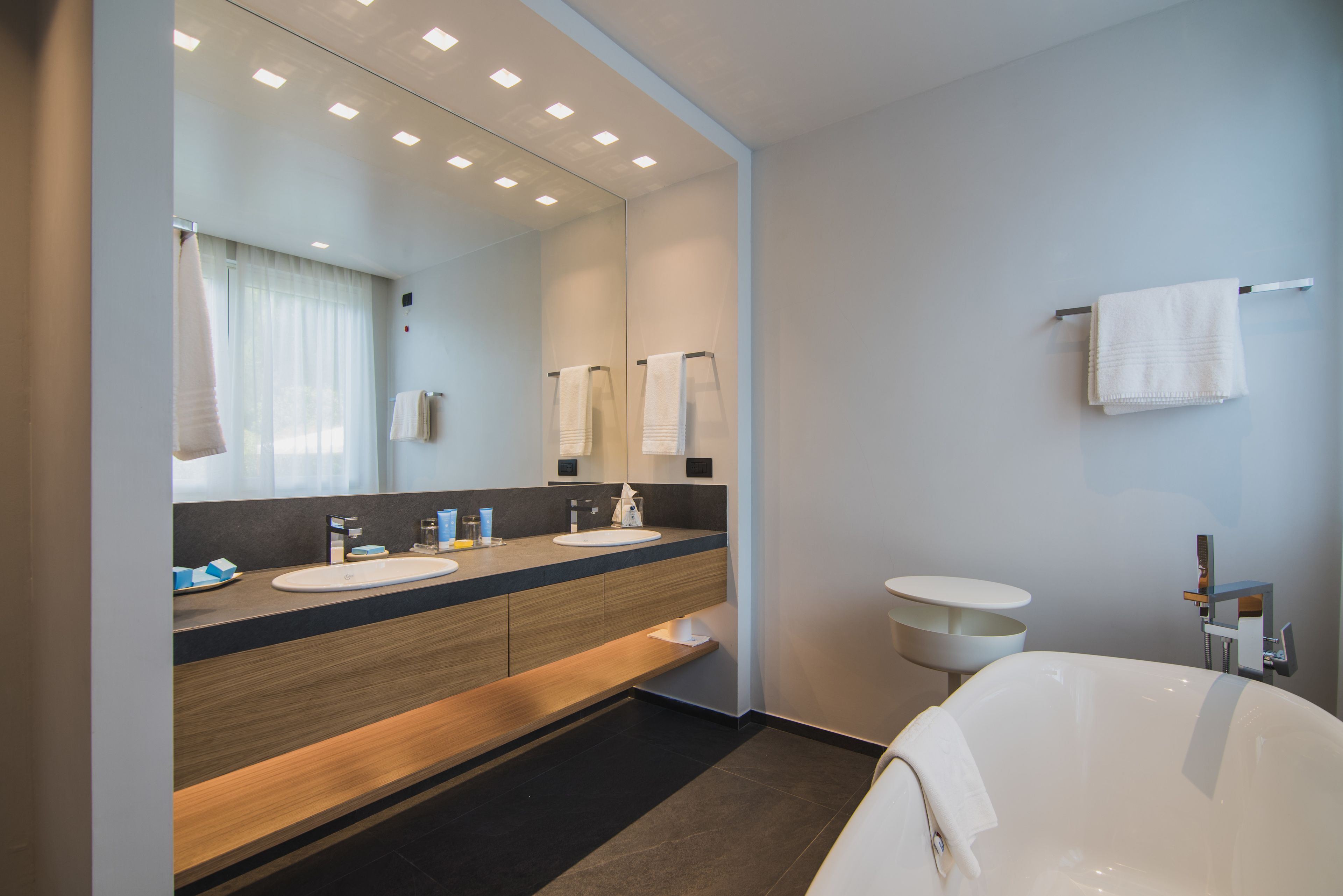 Een moderne badkamer met twee wasbakken, een grote spiegel, een bad en een handdoekrek.