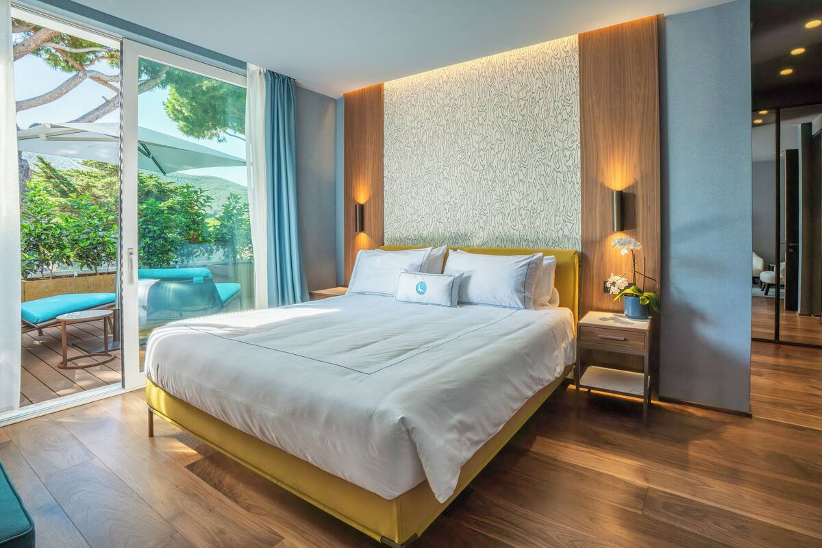 A modern bedroom with a large bed, a wooden floor, and a view of the outdoors.