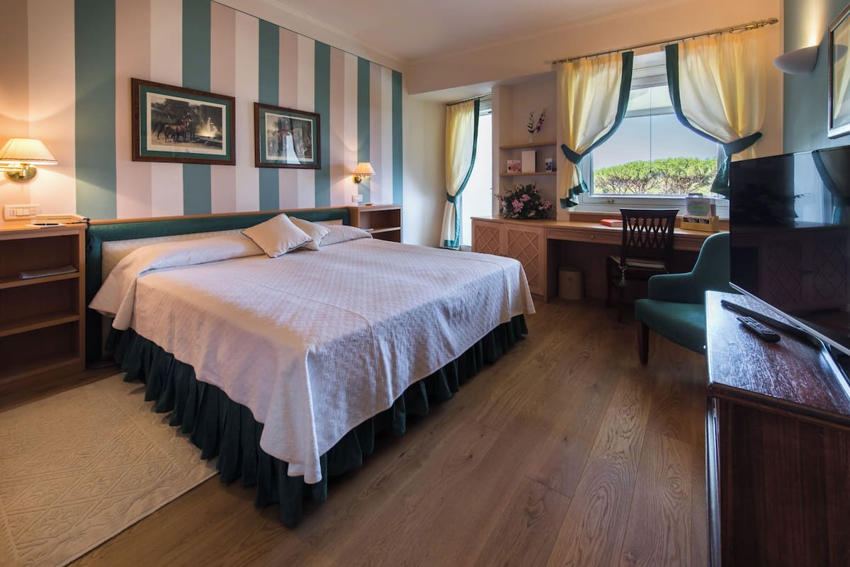 A hotel room with a large bed, a desk with a chair, a television, and a window with curtains.