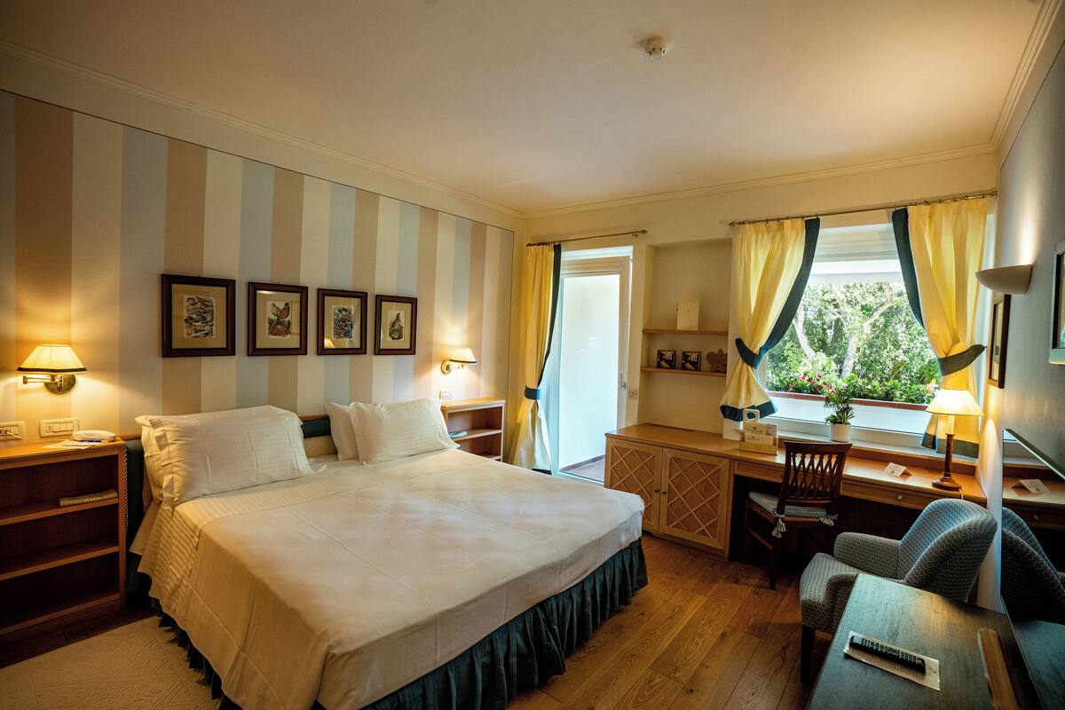 A hotel room with a large bed, a desk, a chair, and a window with curtains.