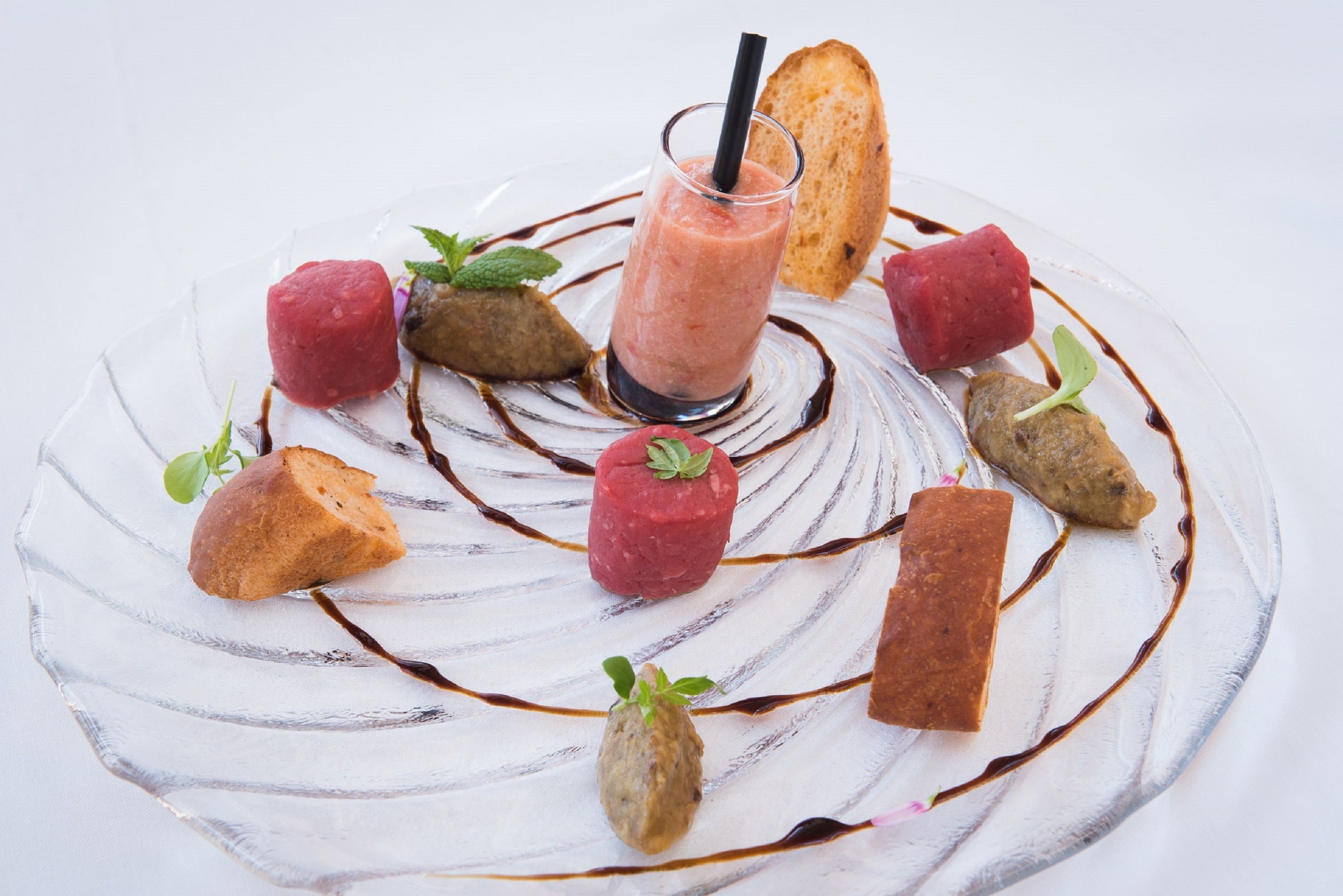 A dessert plate with various items including a glass of a pink beverage, pieces of bread, and small garnishes.