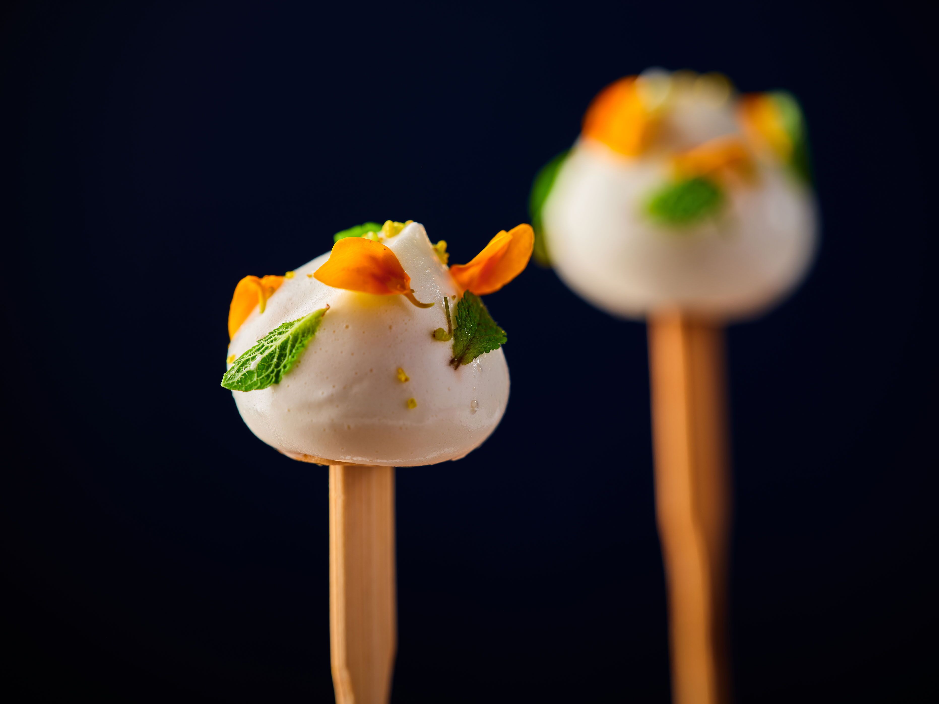Two spherical desserts on sticks with a dark background.