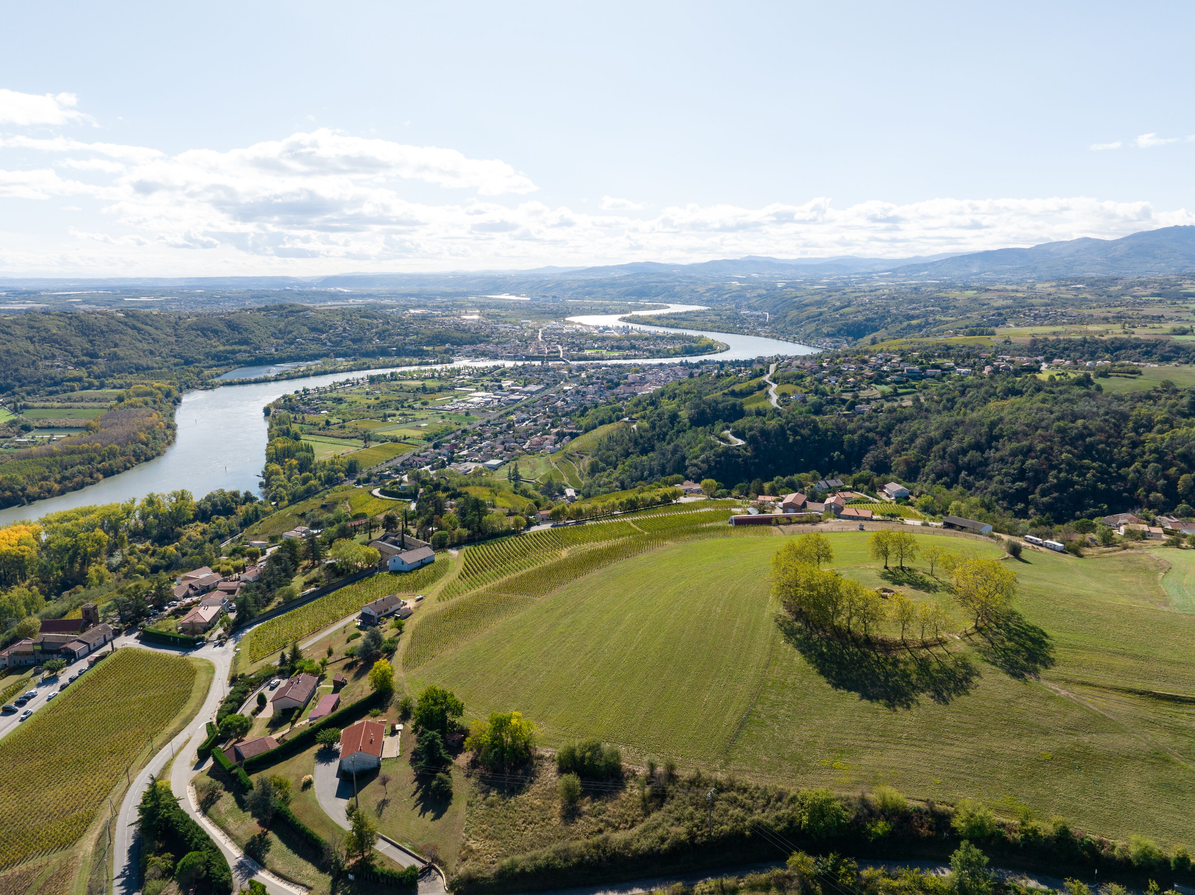 Vista aérea de un pueblo con un río, viñedos y zonas residenciales.