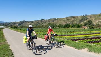 Two cyclists on a paved path with fields and hills in the background.