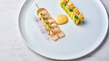 A white plate with two food items: a skewer of meat with a sauce and a row of vegetables with croutons.