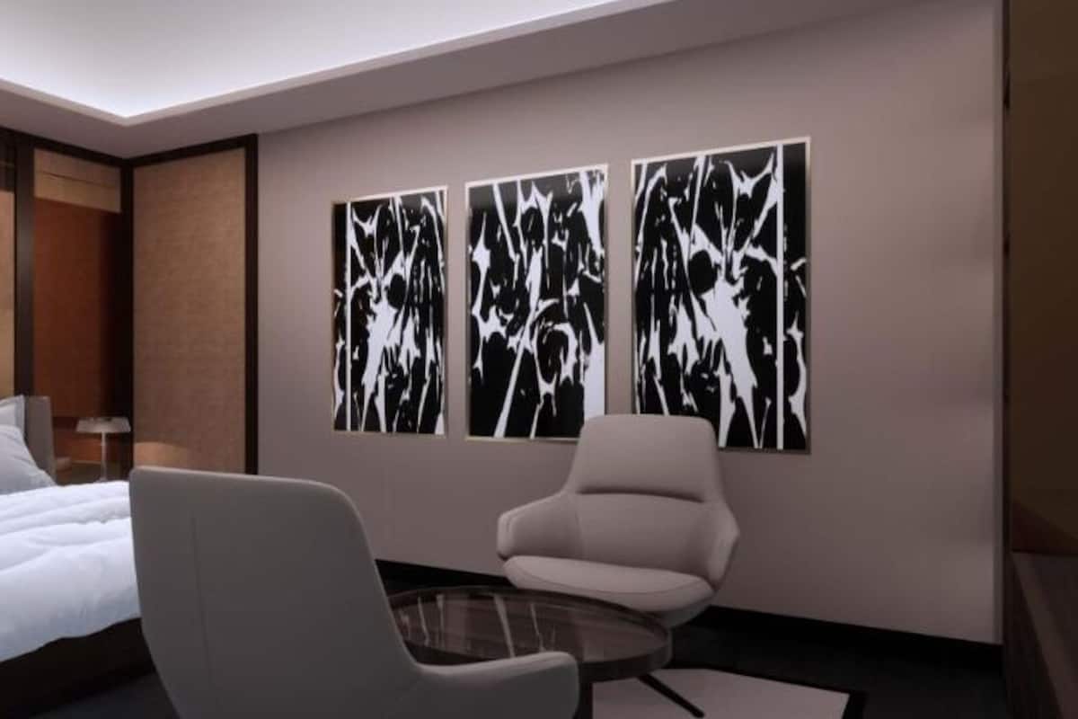 A modern hotel room with a bed, a chair, and abstract wall art.
