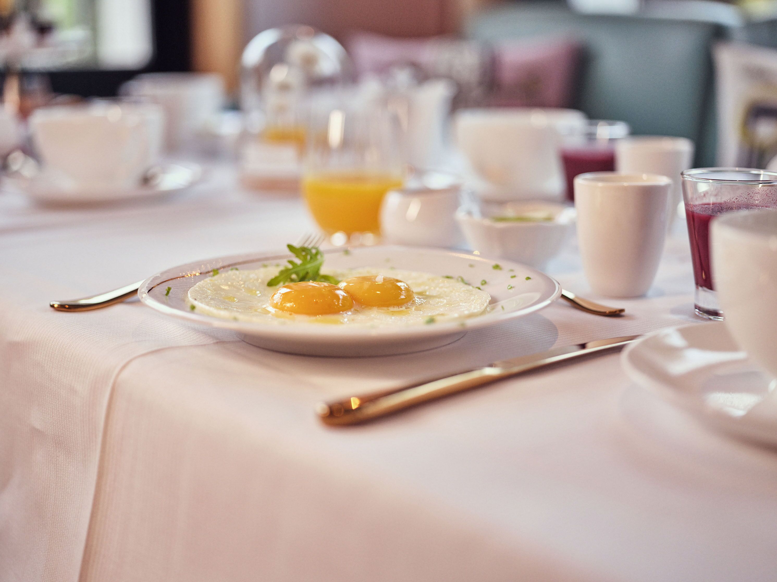 A breakfast setting with a plate of eggs, a glass of orange juice, and various other breakfast items on a table.
