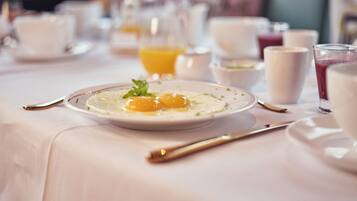 A breakfast setting with a plate of eggs, a glass of orange juice, and various other breakfast items on a table.
